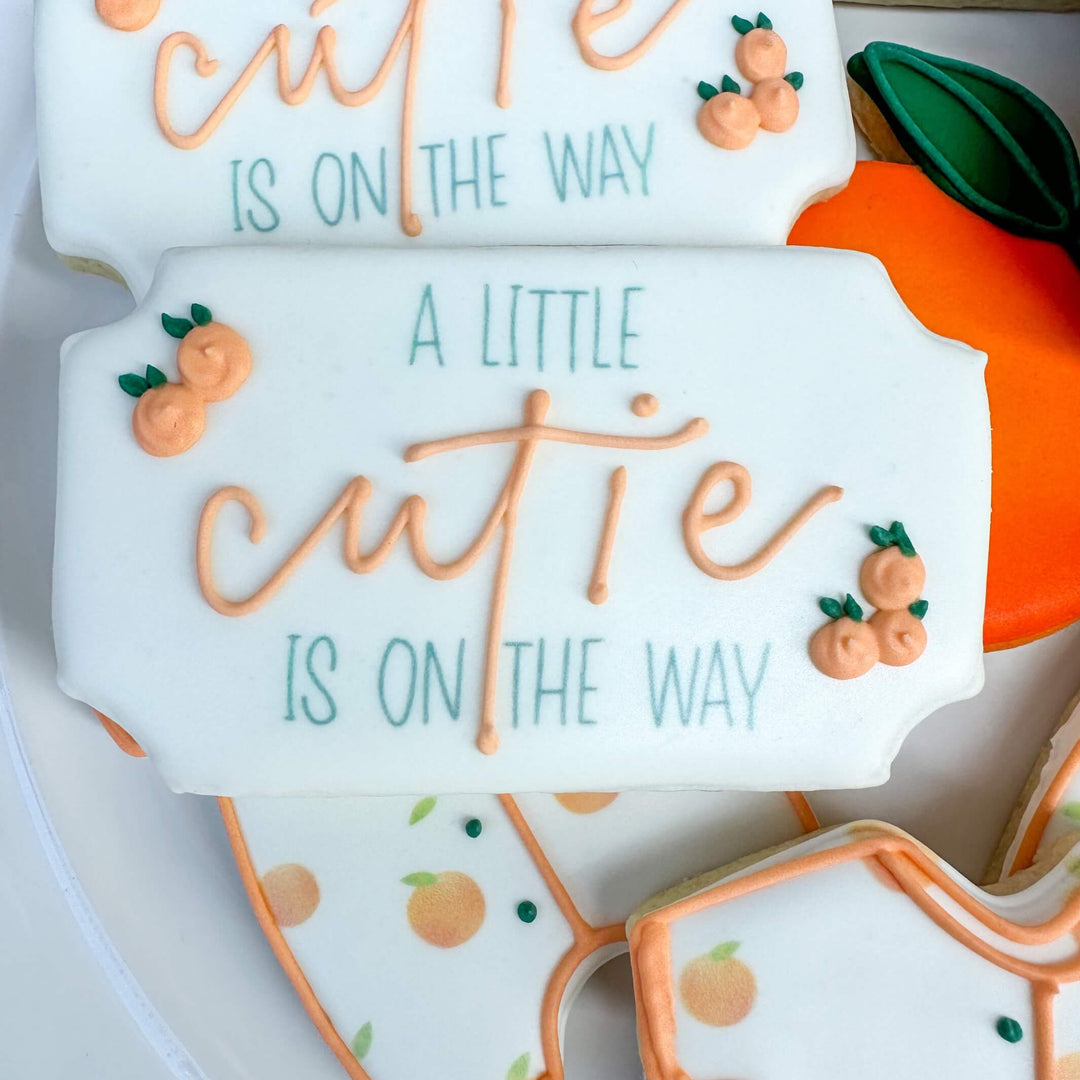 Decorative baby shower cookies featuring cutie phrases and orange designs, perfect for celebrating a new arrival.