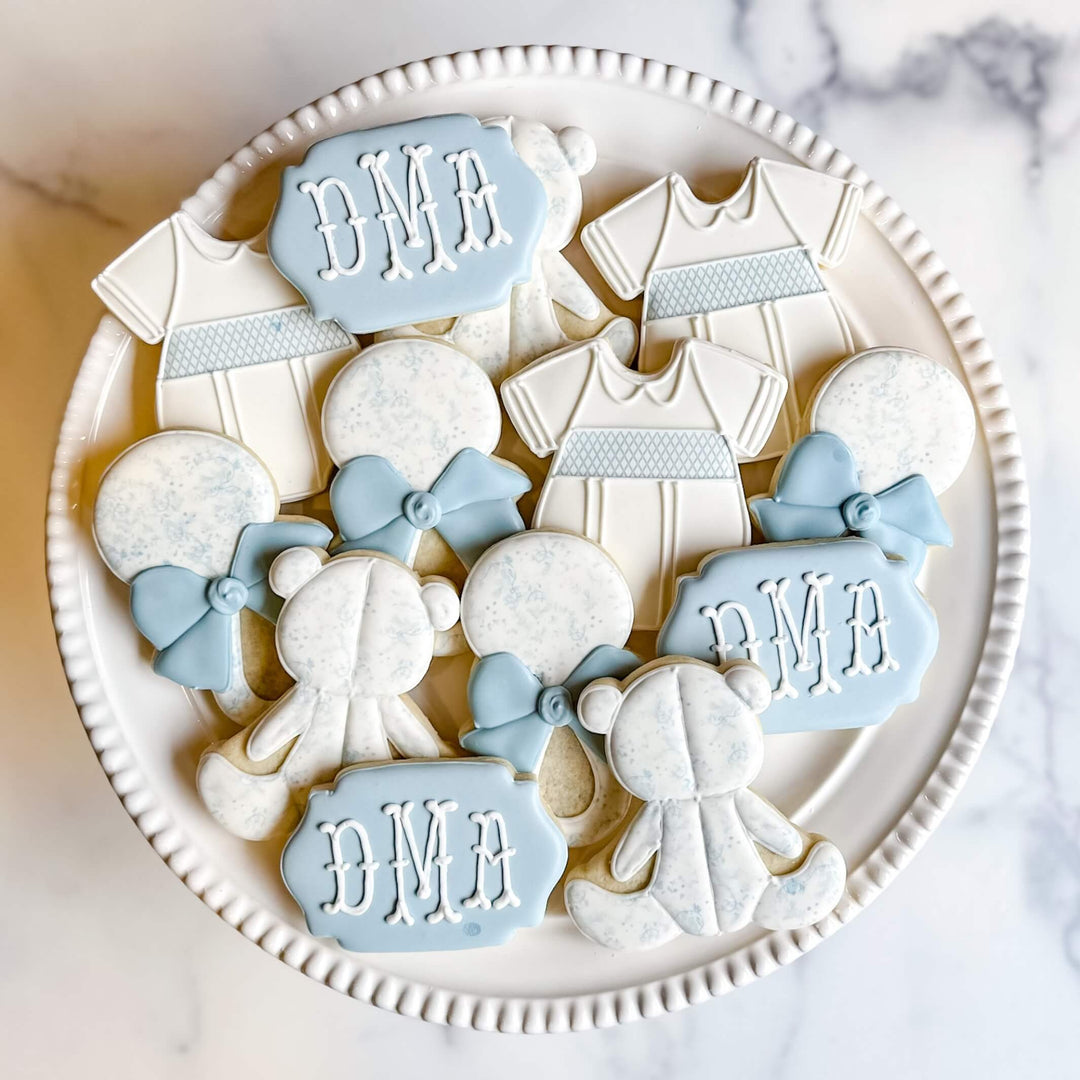 Decorative sugar cookies for boys' events featuring onesies, teddy bears, and monogrammed plaques.