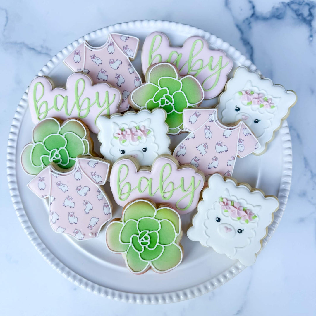 Decorated baby shower cookies featuring llama, baby onesie, and succulent designs, perfect for celebrating new parents.