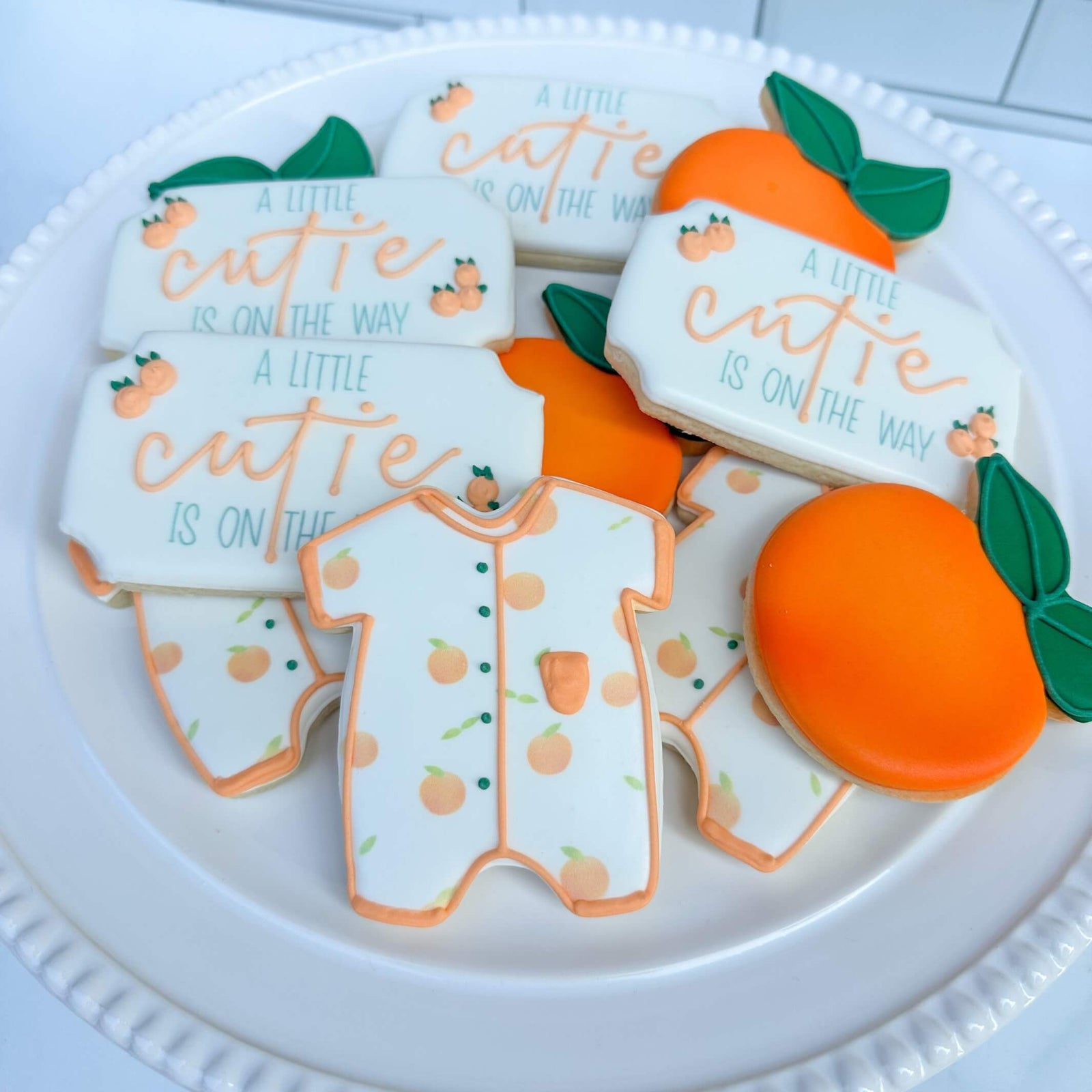 Adorable sugar cookies featuring onesies and oranges for a baby shower, perfect for welcoming a little cutie!