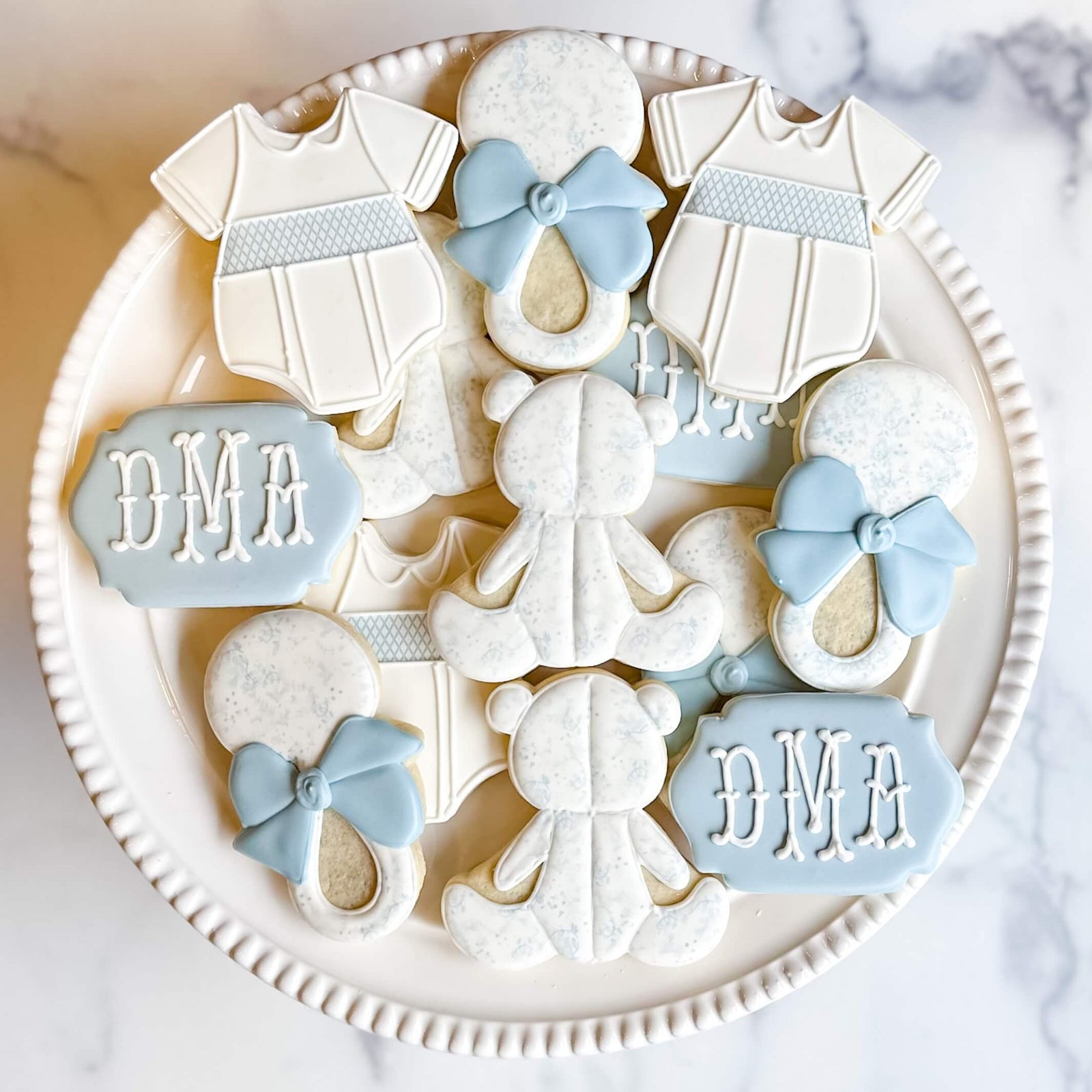 Adorable baby boy sugar cookie set featuring onesies, teddy bears, and monogram plaques on a decorative plate.